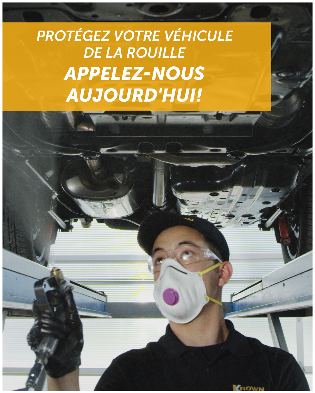 Technicien Krown pulvérisant le revêtement antirouille sous un véhicule soulevé sur un pont élévateur